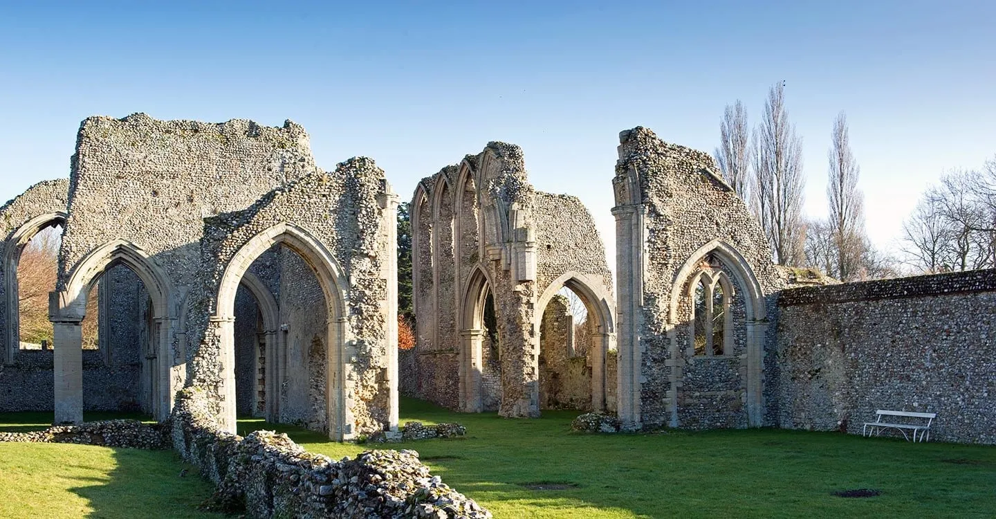 The ruined flint arches and walls of Creake Abbey church on a lawn in bright winter sun, with poplars and a white bench