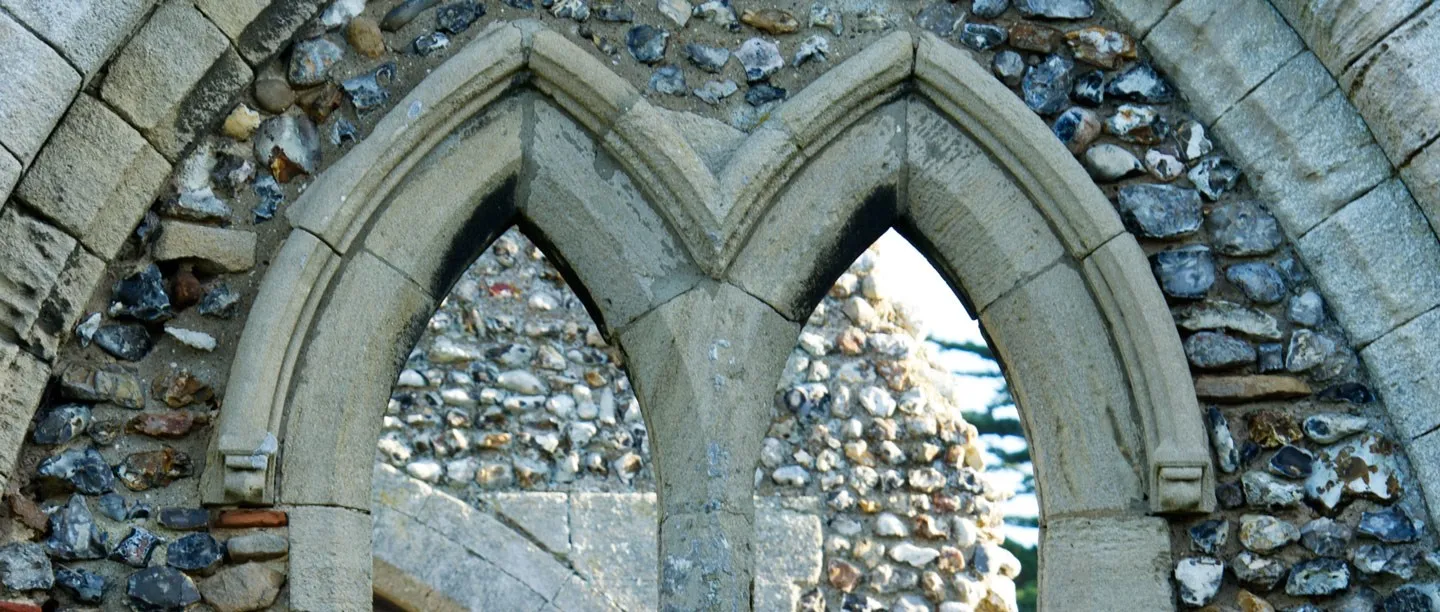 Close-up of a pointed twin window in Creake Abbey's flint walls, with flint ruins seen through the opening