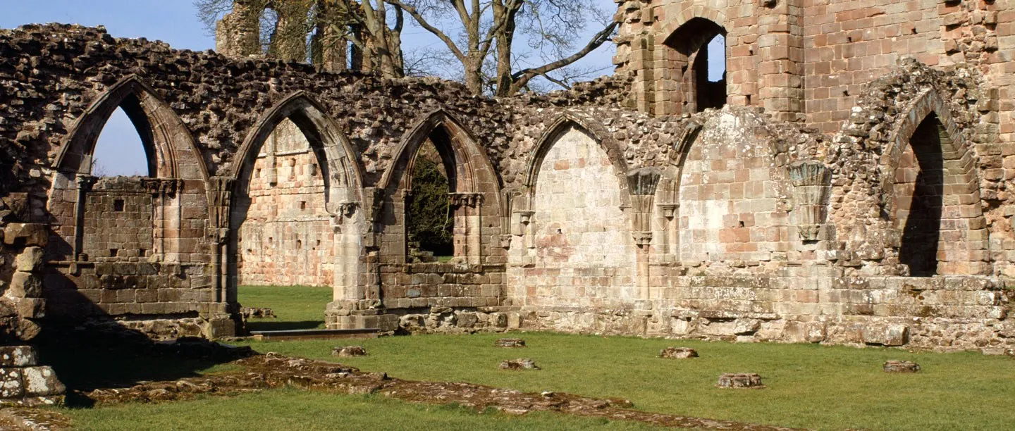 A row of pointed arches into the chapter house of Croxden Abbey, with column bases set in the lawn in front