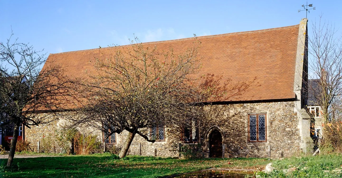 Duxford Chapel, a long flint chapel with a steep red-tiled roof and leaded windows, behind a leaning apple tree on a sunny autumn day