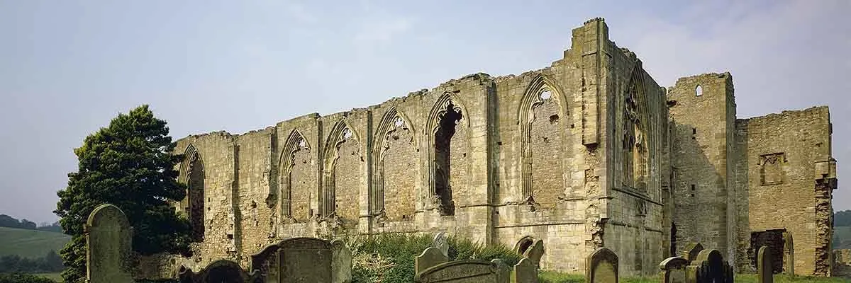 The tall traceried windows of Easby Abbey's refectory above old gravestones in the churchyard