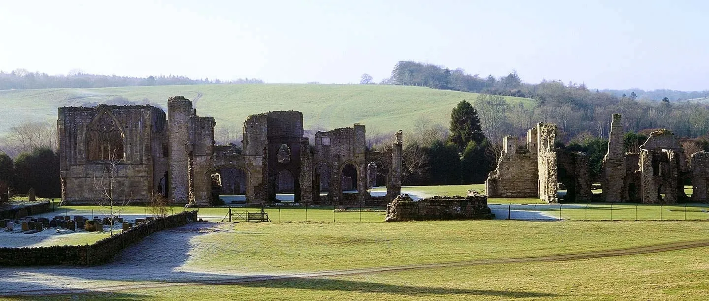 The ruins of Easby Abbey across a frosty lawn, with the churchyard wall and wooded hills behind