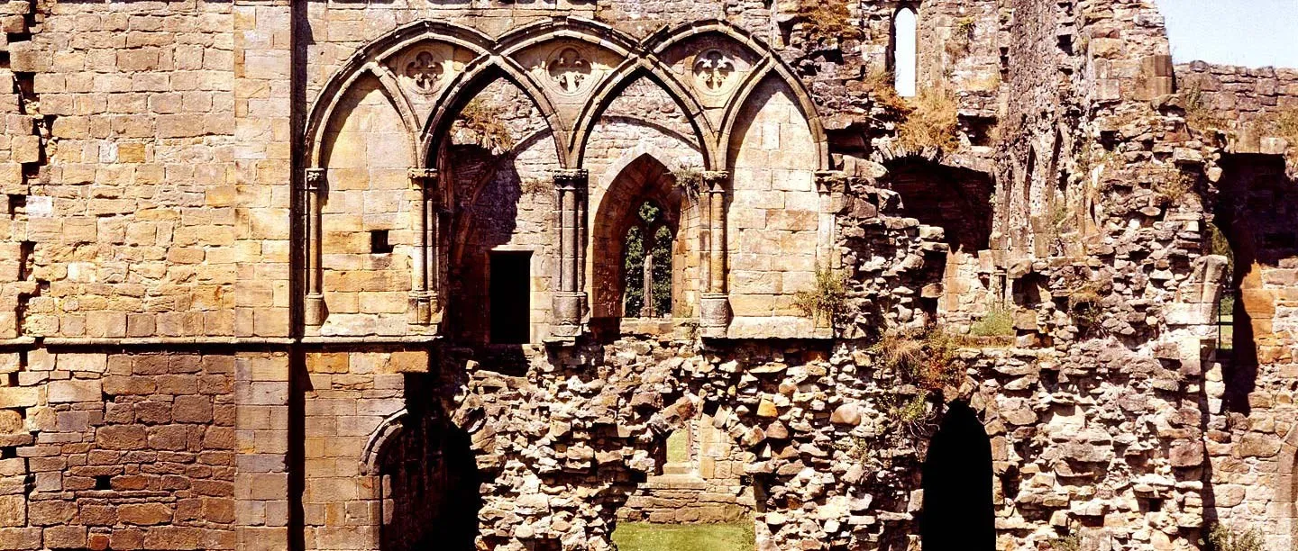 Pointed arches and broken walls of Easby Abbey's cloister buildings in warm sunlight