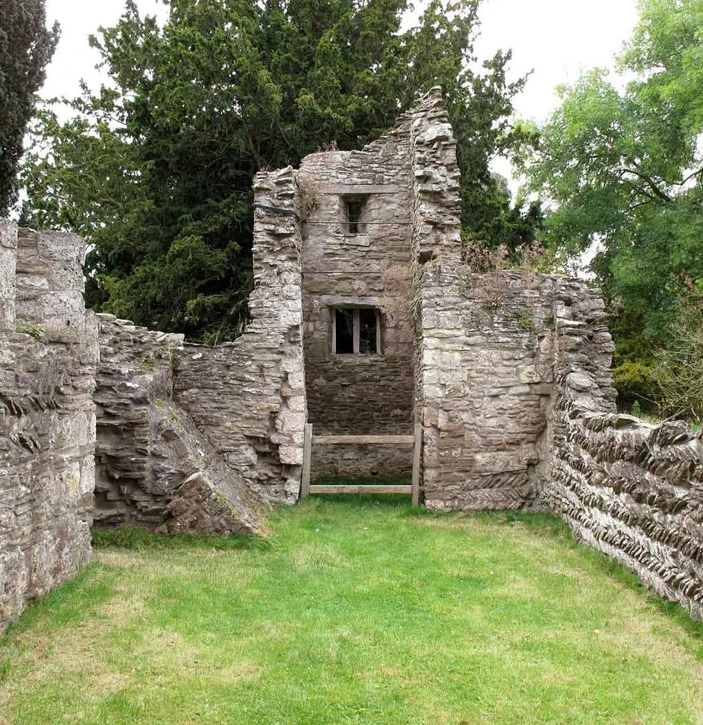 Looking west down the grassed nave of Edvin Loach Old Church between ruined walls to the tower and its window