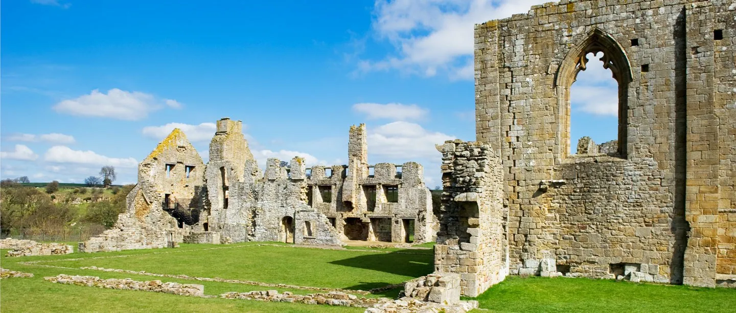 The ruined east range and church walls of Egglestone Abbey across a grassy cloister under a blue sky