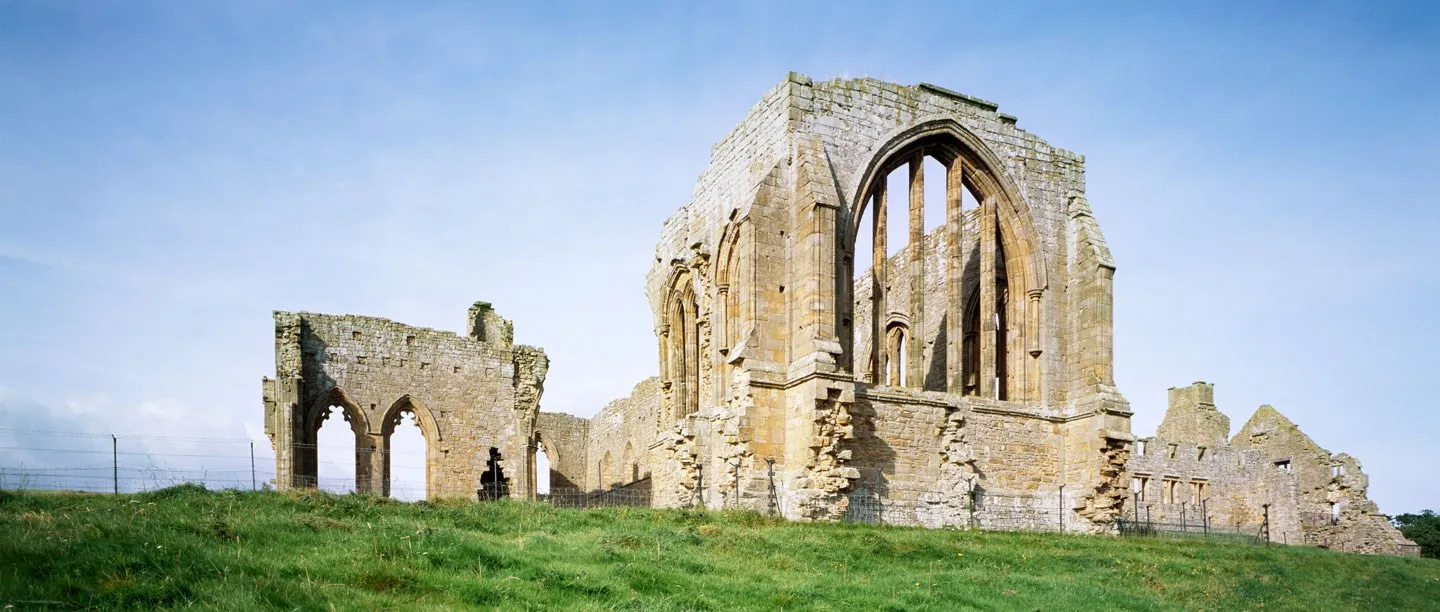 The roofless church of Egglestone Abbey with its tall east window, on a grassy rise