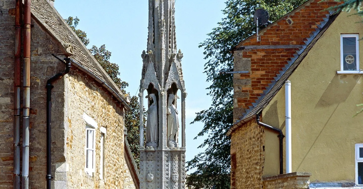 The Eleanor Cross at Geddington, with carved statues of Queen Eleanor in its canopied niches, between stone houses