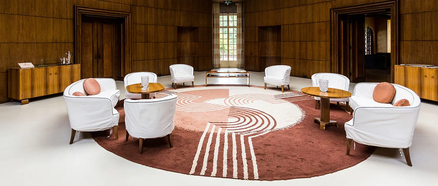 The Art Deco entrance hall with white armchairs on a circular rug