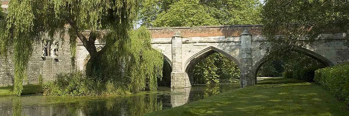 The medieval stone bridge over the moat framed by a weeping willow