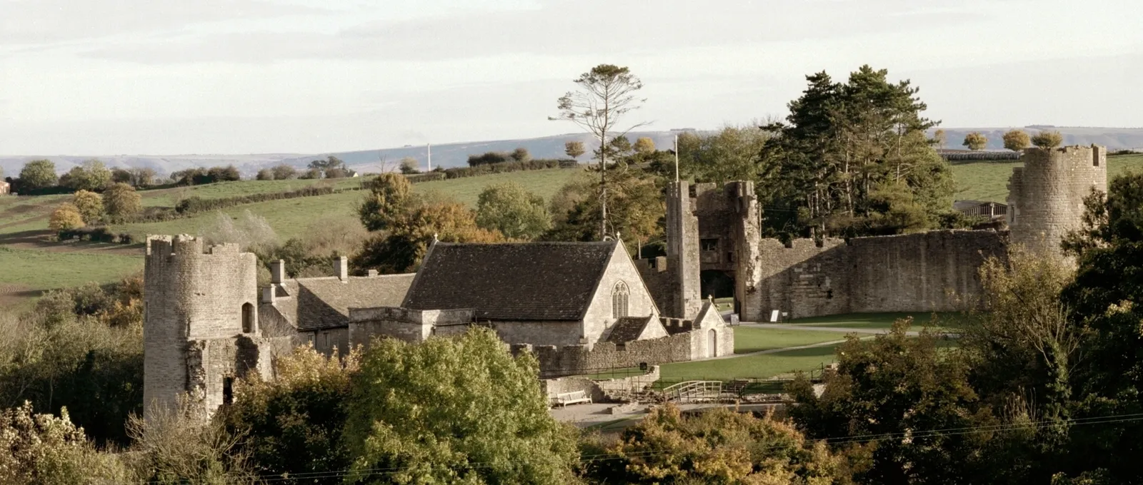 Farleigh Hungerford Castle from the hillside in autumn, with its towers, chapel and curtain wall among trees