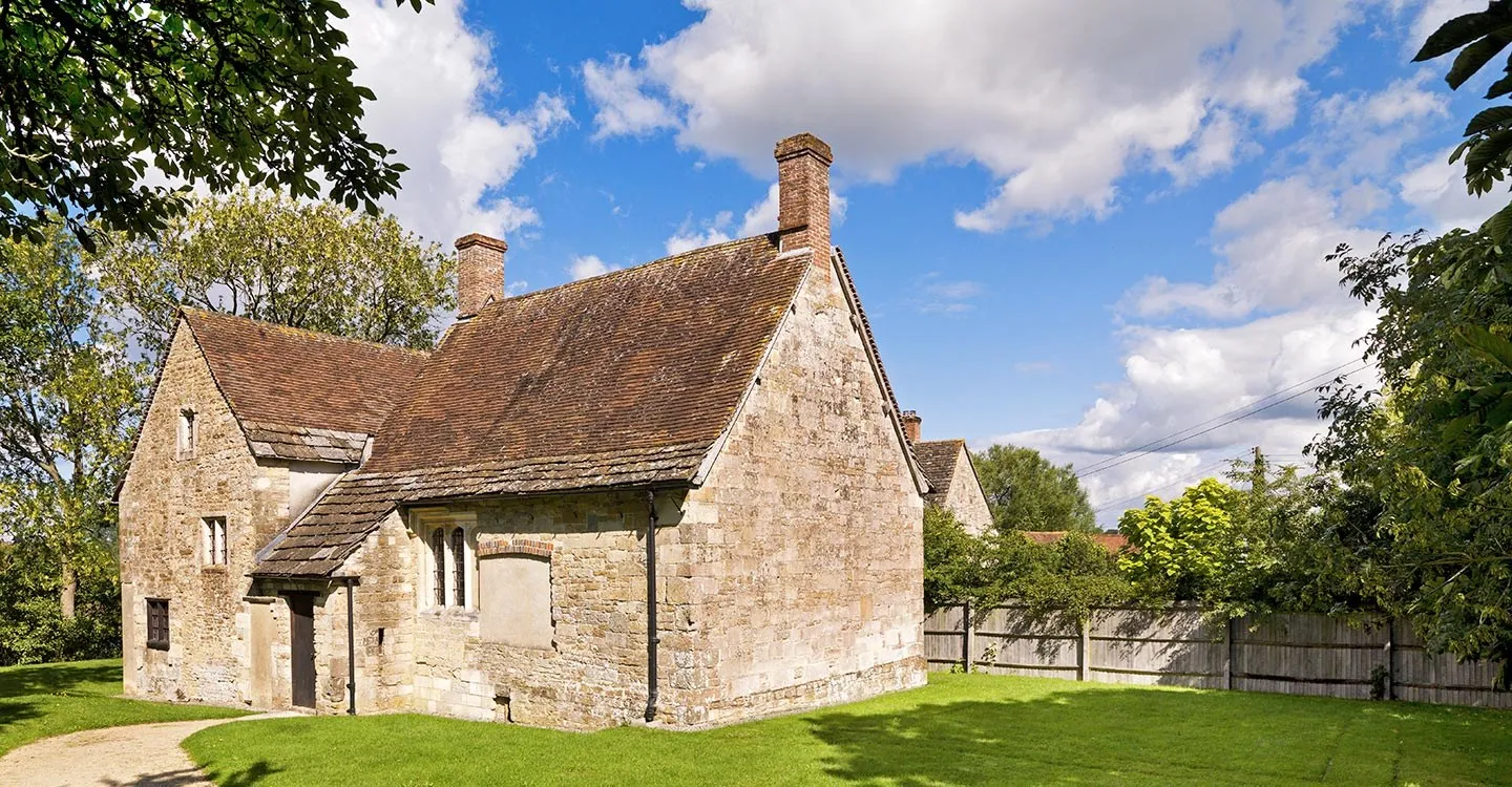 Fiddleford Manor, a medieval stone house with a tiled roof and brick chimneys on a sunny summer day