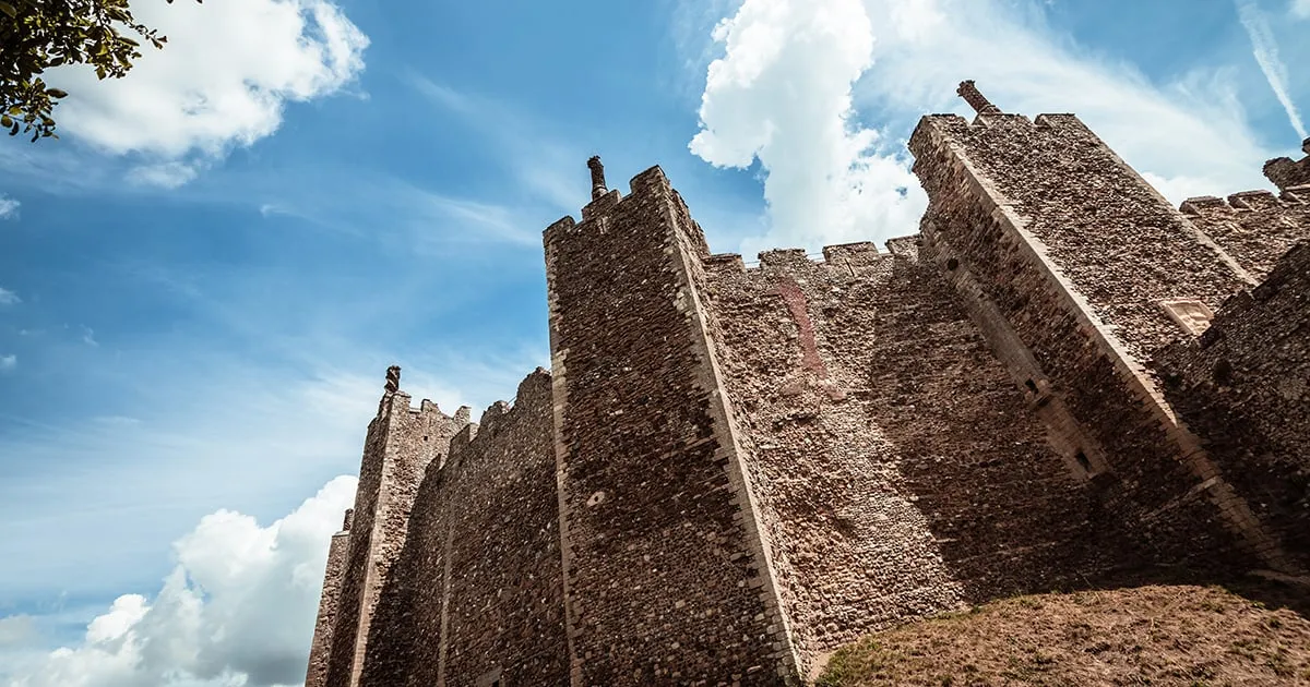 Looking up at the flint curtain wall and towers against a summer sky