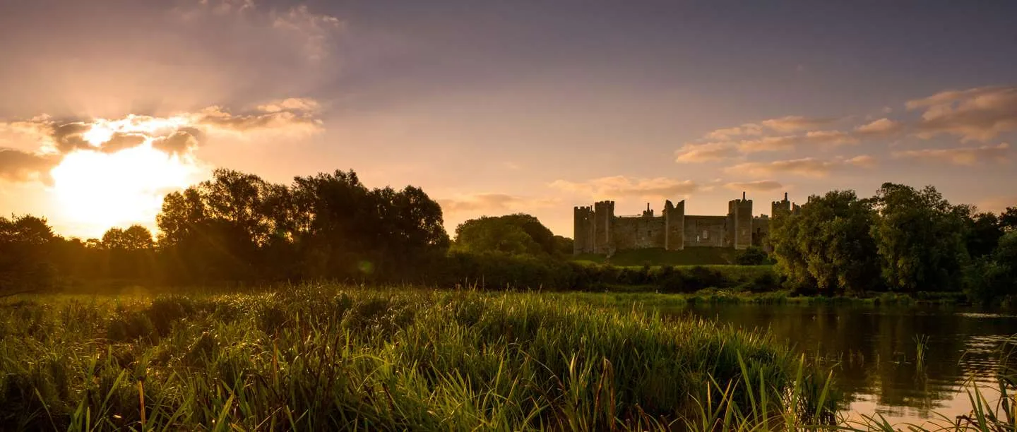 The castle silhouetted at sunset across the reed-fringed mere