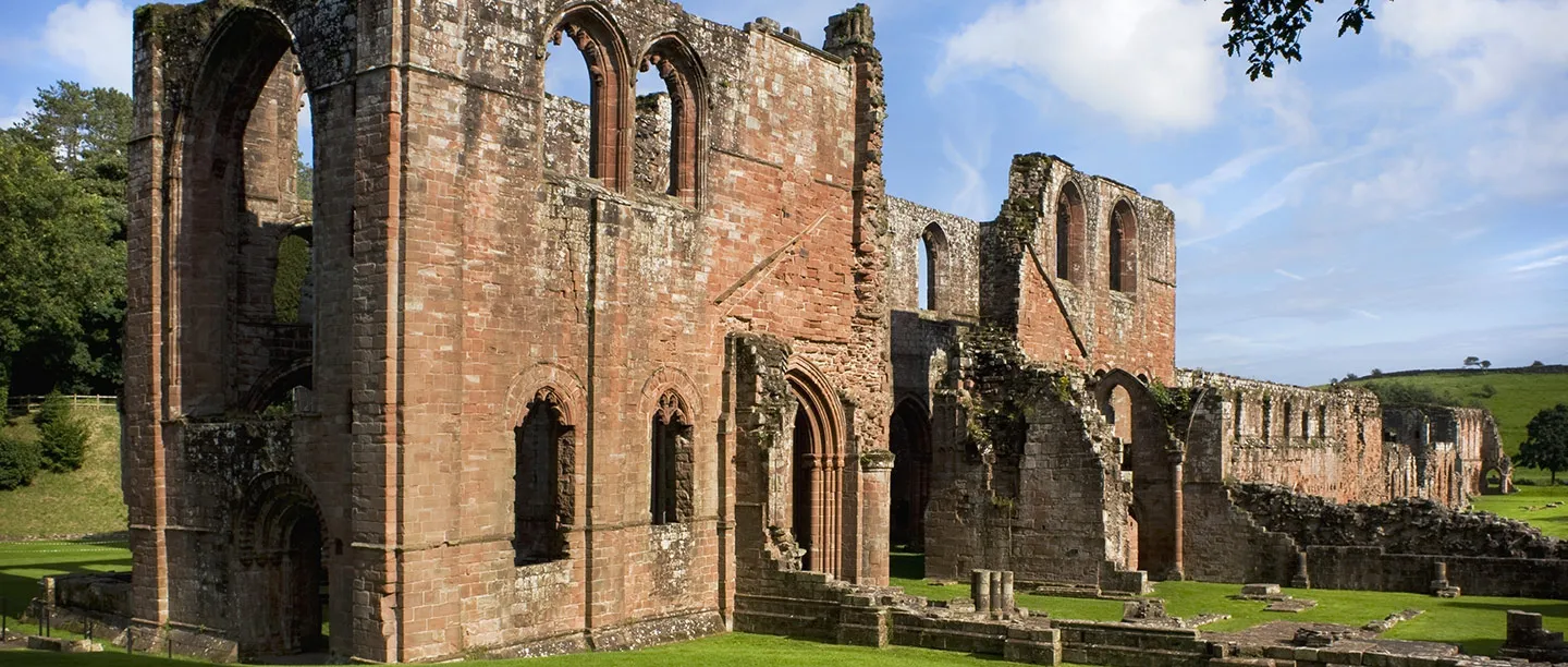 The red sandstone walls and tall arches of Furness Abbey's church and transept under a summer sky