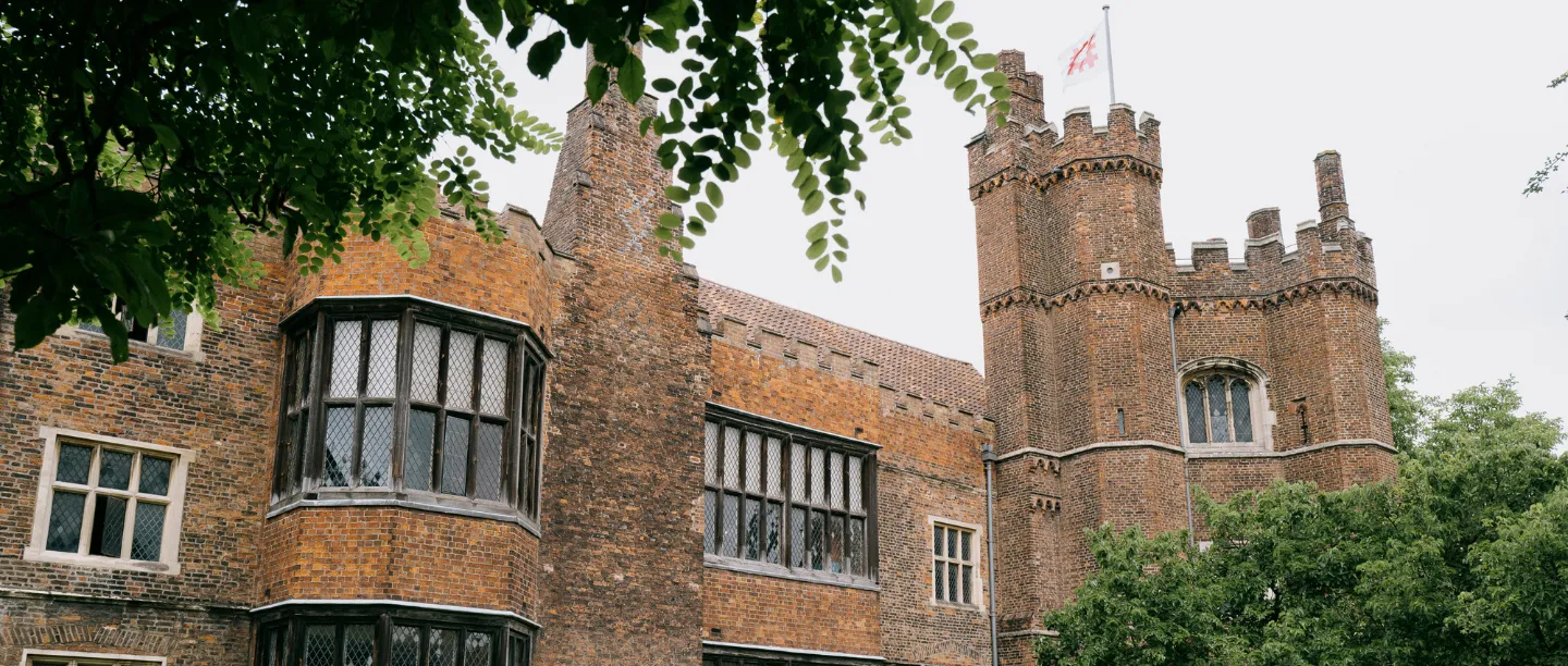 The battlemented tower and an oriel window framed by leaves