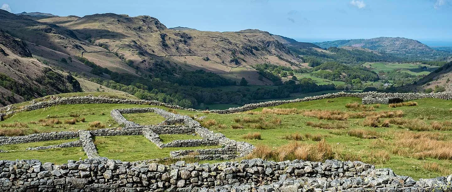 Low stone walls of the headquarters at Hardknott Roman fort, with Eskdale's fells and woods beyond