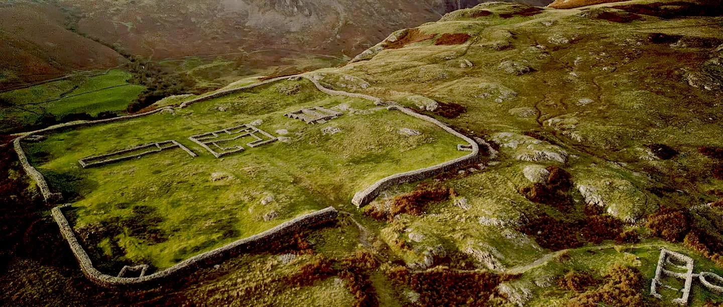 Aerial view of Hardknott Roman fort's walls and buildings on a green spur above the valley
