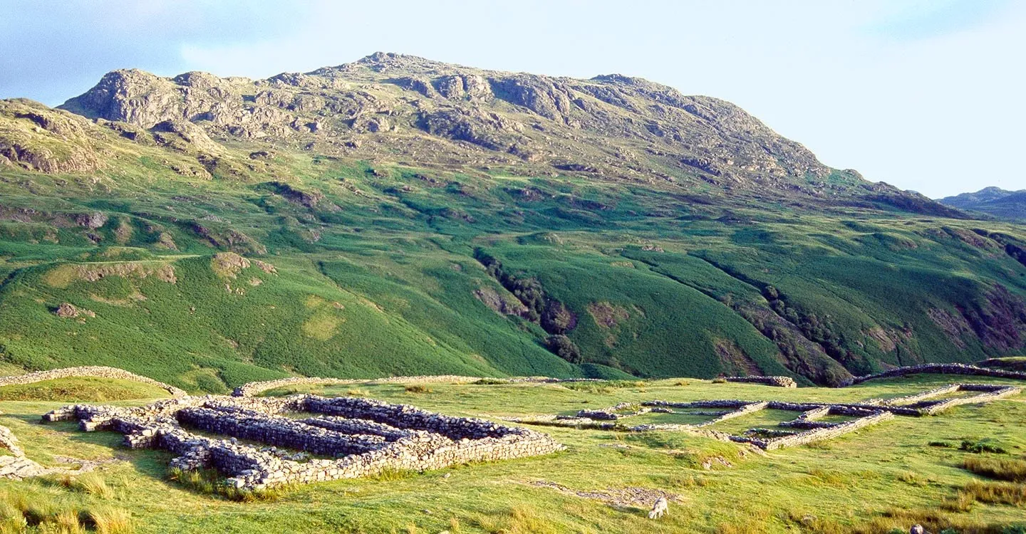 Footings of the headquarters at Hardknott Roman fort in evening light, below the crags of Hard Knott