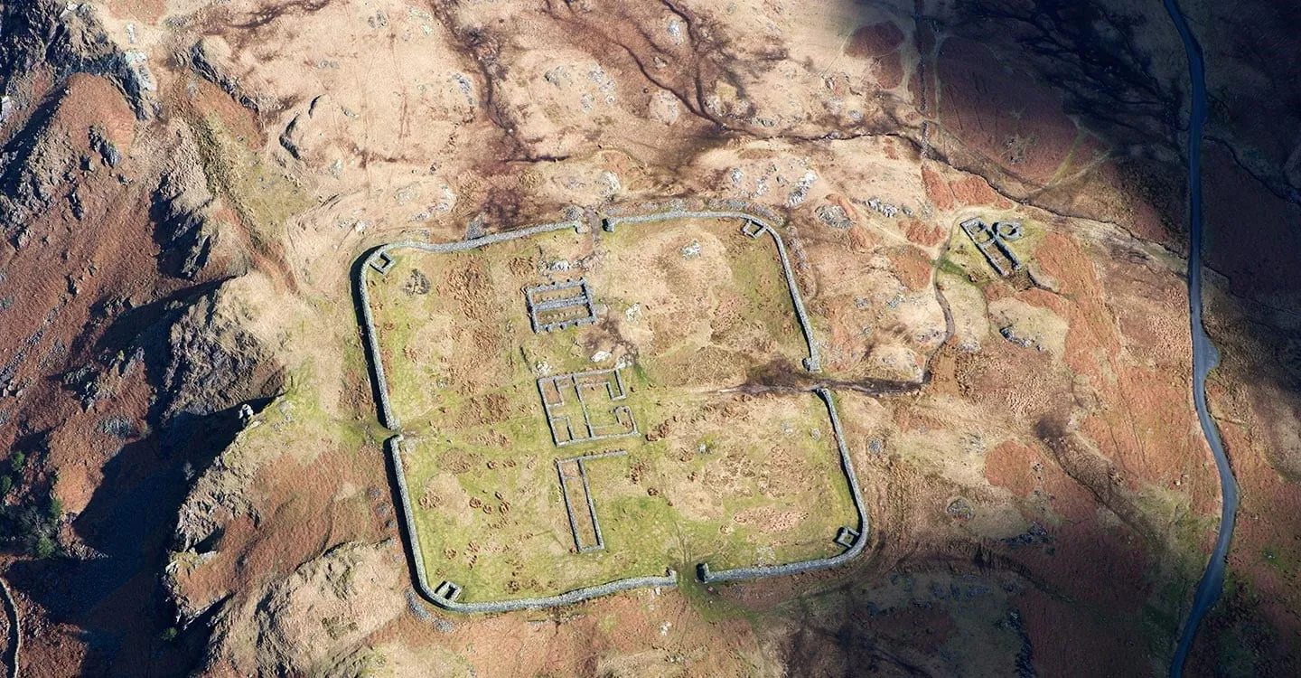 Vertical aerial view of Hardknott Roman fort's square walls and bath house on the fellside, with the pass road beside it