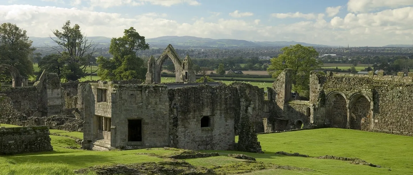 The ruined abbot's lodging and cloister buildings of Haughmond Abbey with trees and the Welsh hills beyond