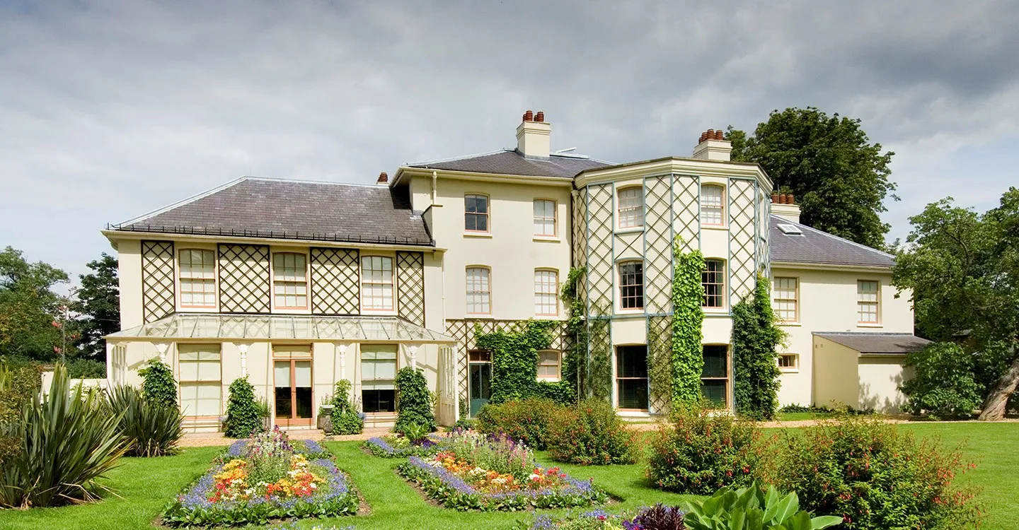 The rear of Down House, with its trellised veranda and bay, above summer flower beds