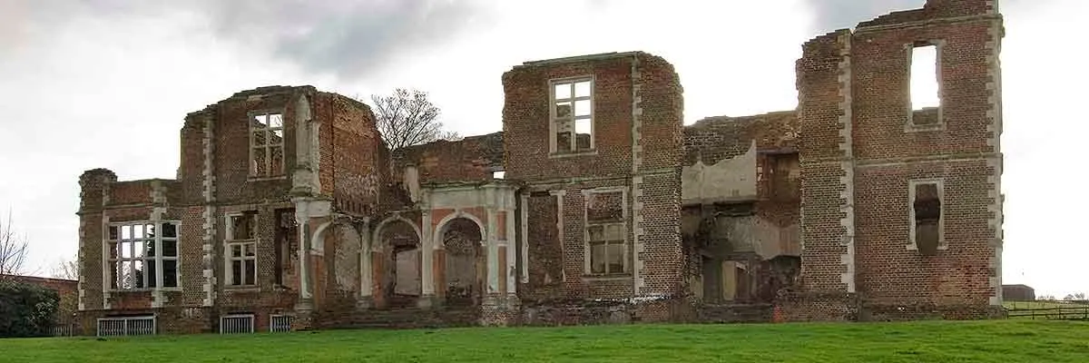 The ruined north front of Houghton House with its arched stone loggia and tall brick walls under a grey sky