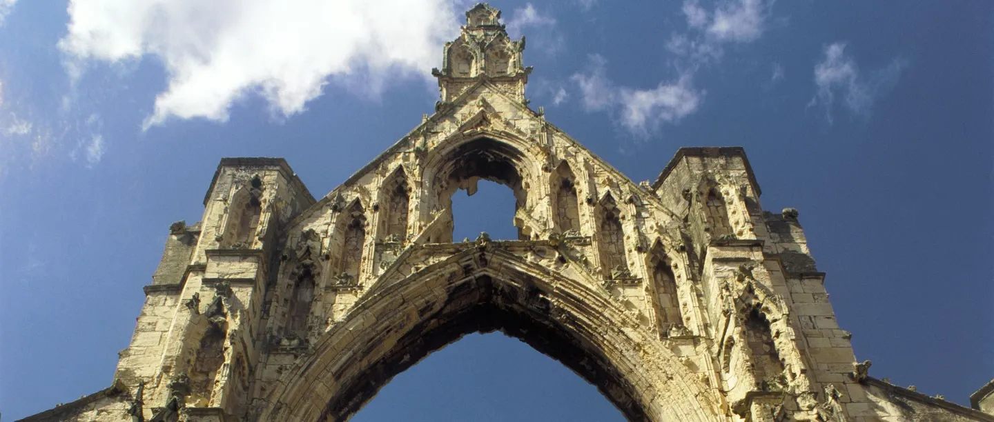 The ruined east gable of Howden Minster's chancel, a great pointed arch beneath pinnacles and canopied niches, against a blue sky