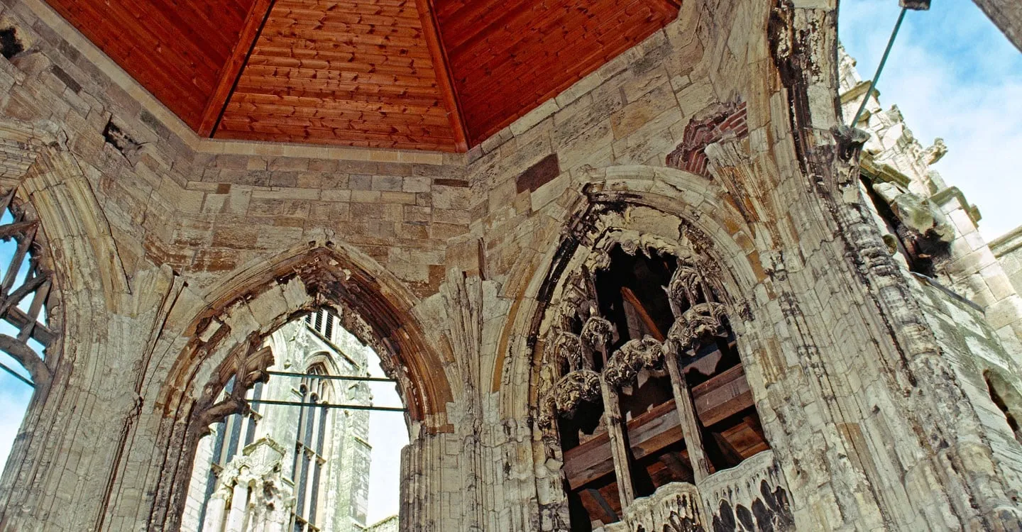 Inside the ruined chapter house at Howden Minster, crumbling carved canopies and window tracery under a timber roof
