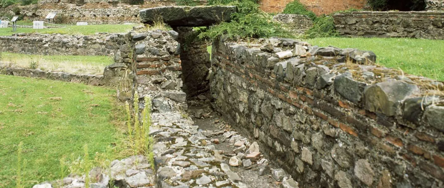 A Roman drain beneath a stone capstone among the low walls of the bath house at Jewry Wall, on green lawns