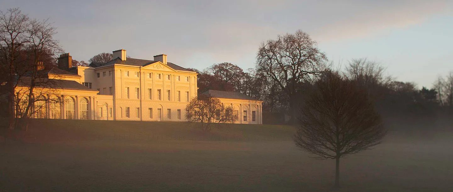 The south front lit gold at sunrise above a misty lawn