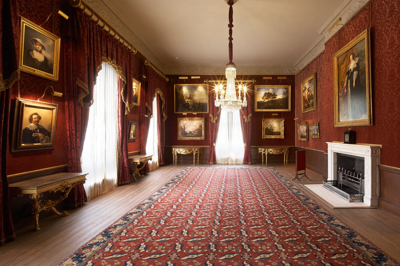 A damask-hung picture room with paintings, a chandelier and a marble fireplace