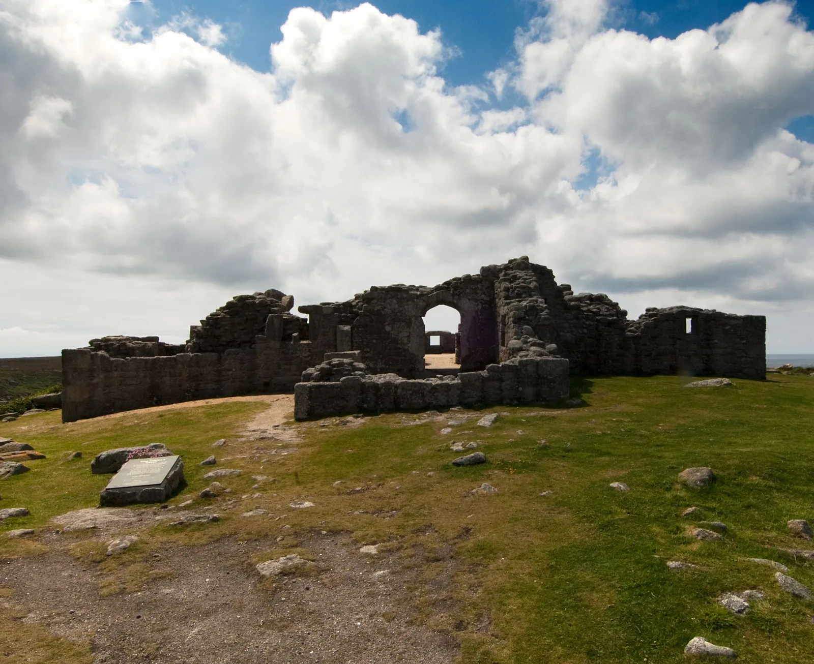 The entrance front of King Charles's Castle, a rubble granite ruin with an arched doorway, on a grassy hilltop with an interpretation panel