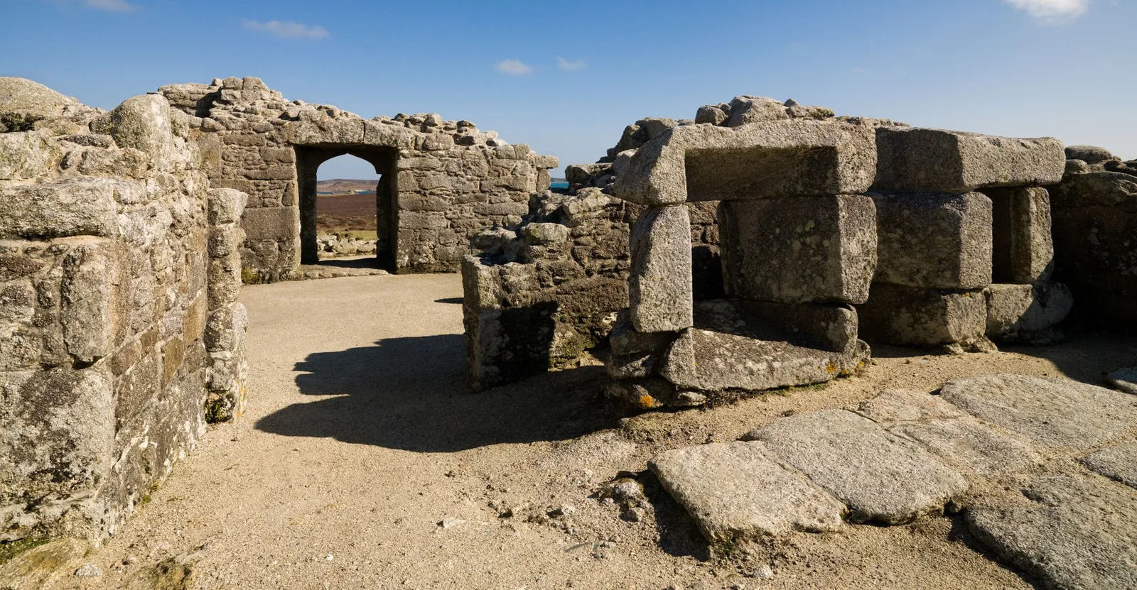 Inside King Charles's Castle, a pointed doorway framing the heath beyond, with massive granite blocks and a sandy floor