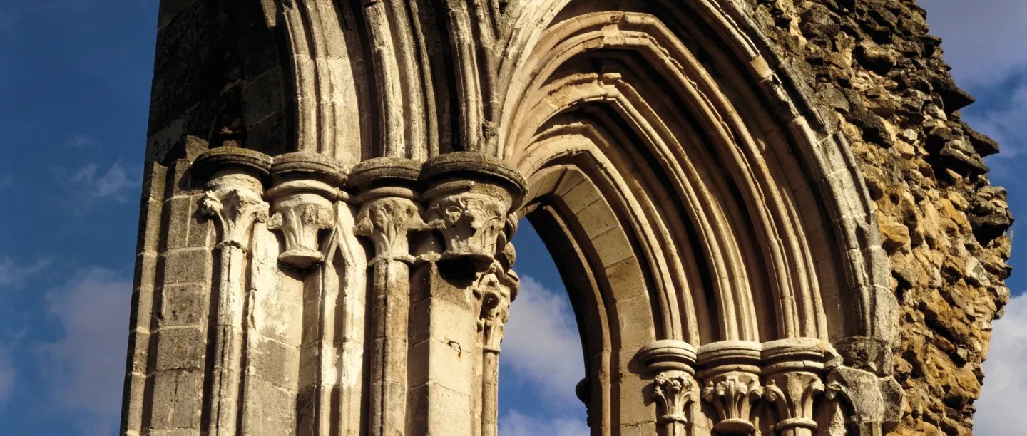 Carved stone capitals and mouldings of a Gothic arch at Kirkham Priory against a deep blue sky