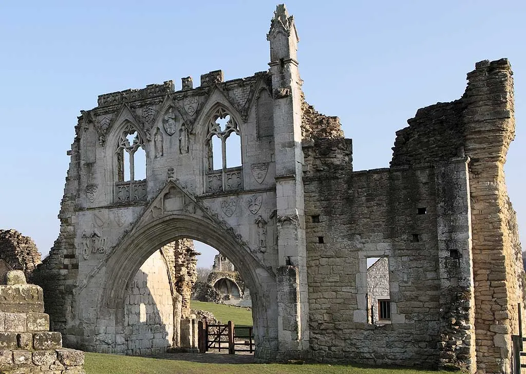 The carved gatehouse arch of Kirkham Priory in spring sun, with the priory ruins seen through the archway