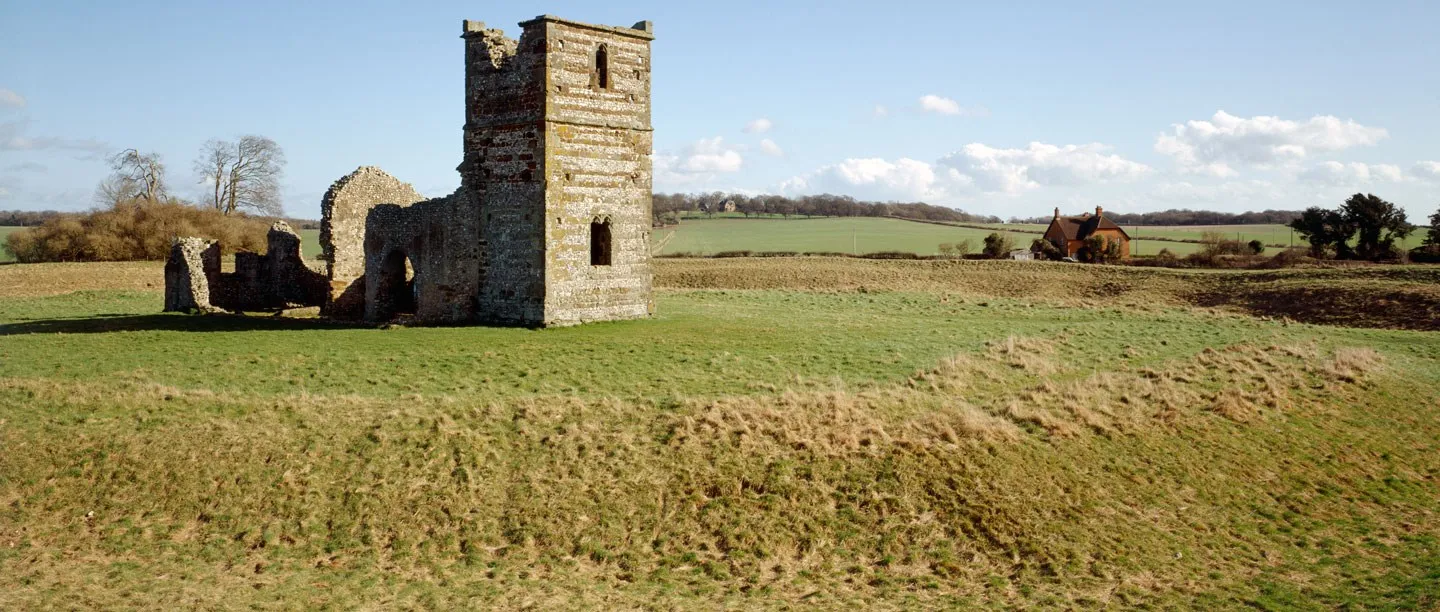 The ruined Norman church at Knowlton standing inside the grassy bank of a prehistoric henge, with a farmhouse and fields beyond