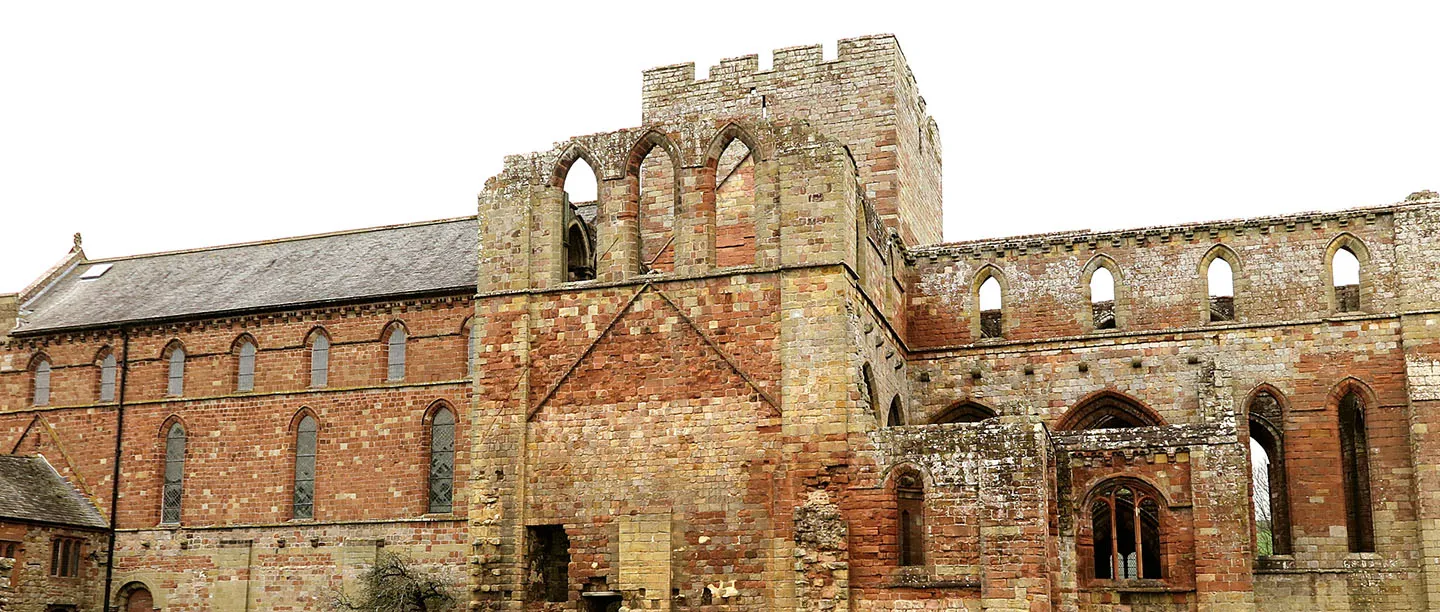 Lanercost Priory's red sandstone nave and ruined chancel under a pale sky