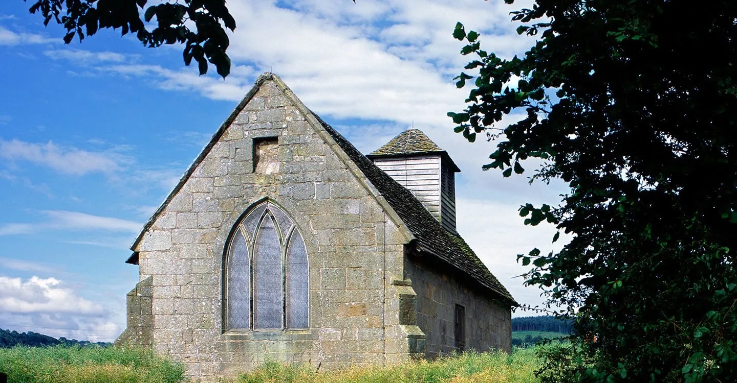 Langley Chapel's stone east gable with a three-light Gothic window and small timber bell turret, framed by dark trees