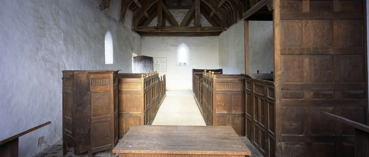 The whitewashed interior of Langley Chapel with plain oak box pews, a reading desk and an open timber roof
