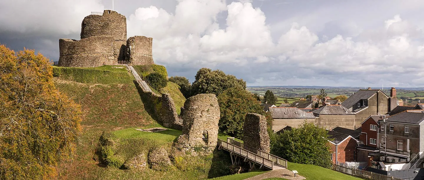 The keep on its motte, ruined gatehouse towers and a wooden footbridge at Launceston Castle above the town rooftops