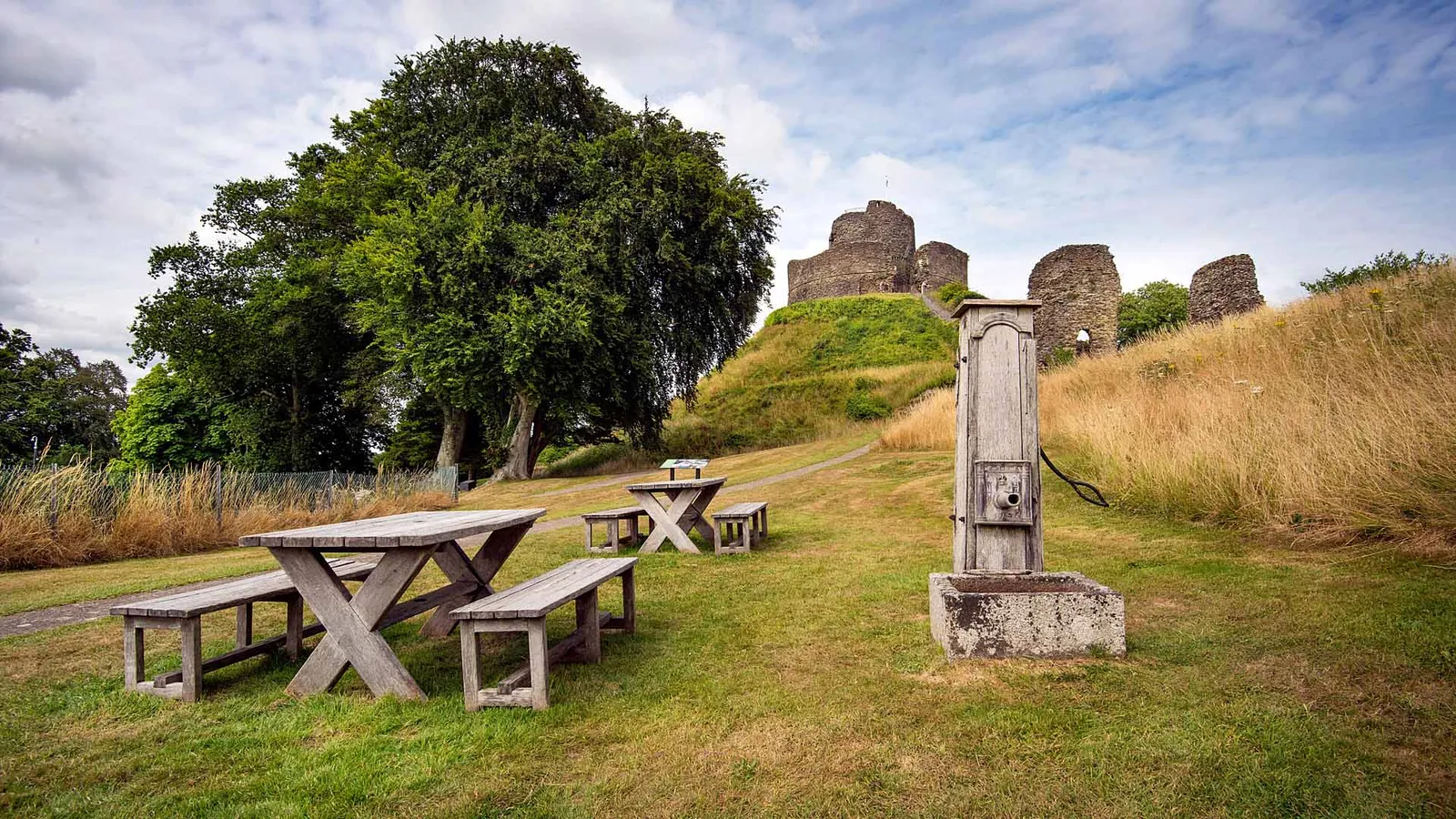 Wooden picnic tables and an old water pump on the lawn below Launceston Castle's keep and towers
