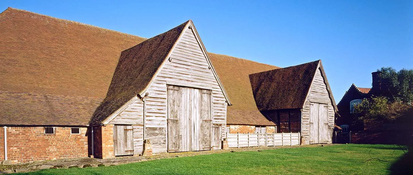 Leigh Court Barn's vast red-tiled roof and two weatherboarded porches with tall doors, above a green lawn under a blue sky
