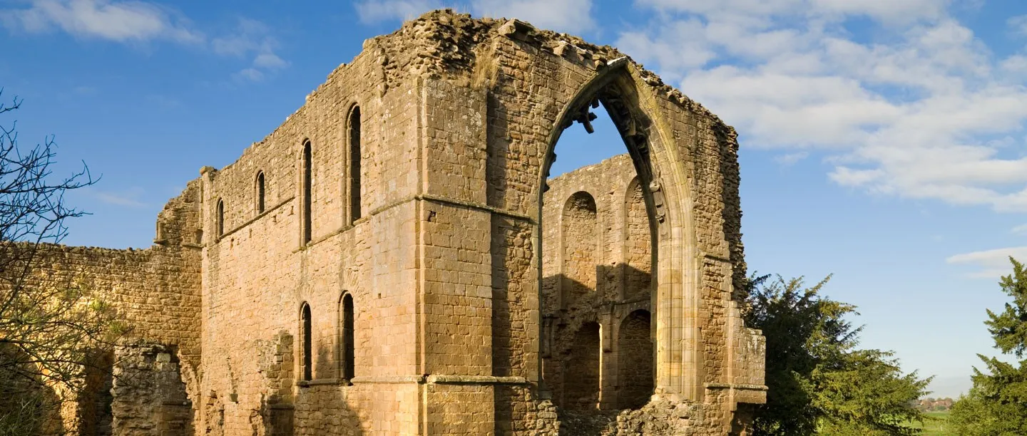 The tall sandstone walls of Lilleshall Abbey church with a great pointed window arch open to the blue sky