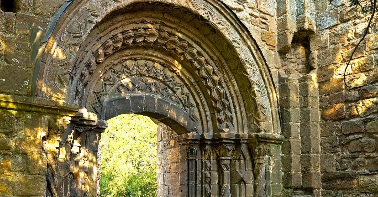 The richly carved Norman processional doorway at Lilleshall Abbey, with zigzag mouldings and twisted columns lit by low sun