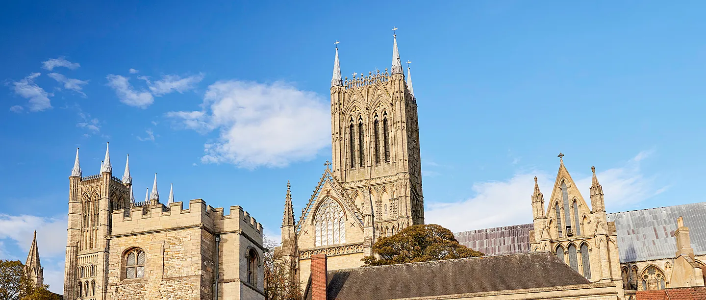 The palace's battlemented tower beside the central tower and gables of Lincoln Cathedral under a blue sky