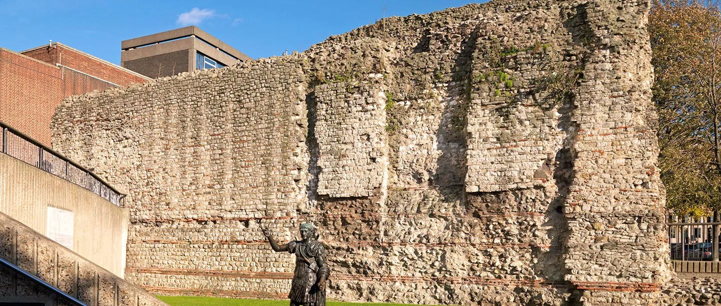 A tall stretch of the Roman and medieval London Wall at Tower Hill, with the bronze statue of Trajan in front
