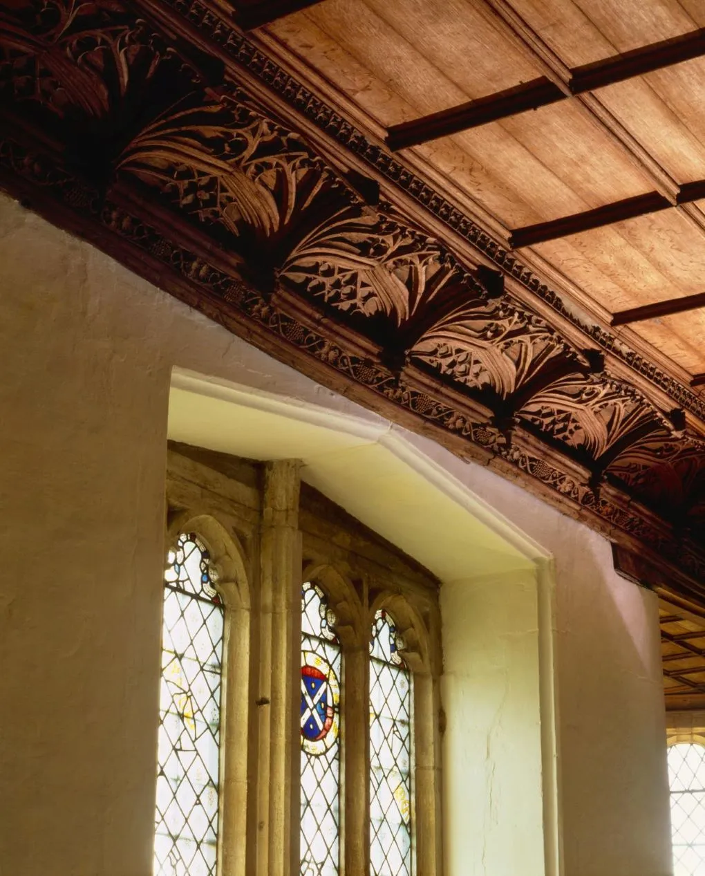 The carved oak cornice and boarded ceiling of the great chamber at Lyddington Bede House, above a leaded window with a heraldic shield