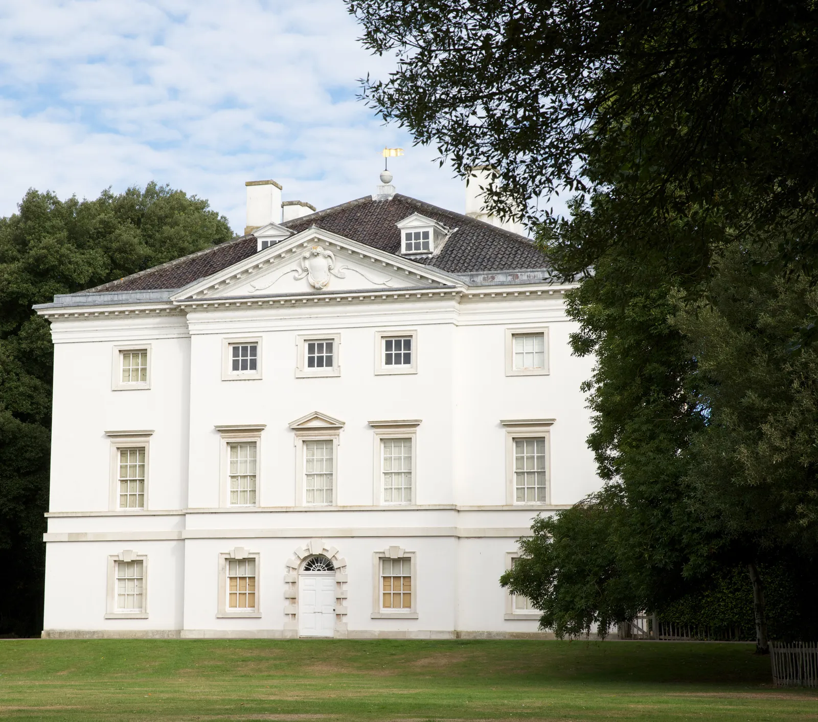 The white Palladian north front of Marble Hill with its pediment and weathervane, across a wide lawn under a blue sky
