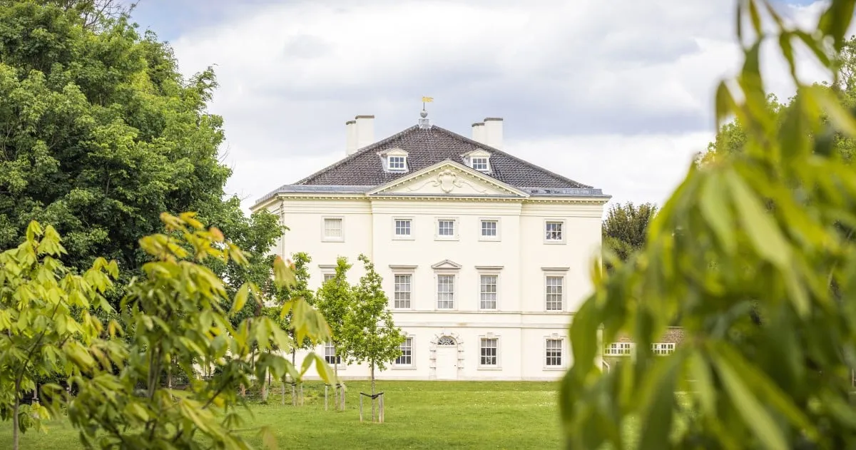 Marble Hill's white villa beyond young chestnut trees on the lawn under a cloudy sky