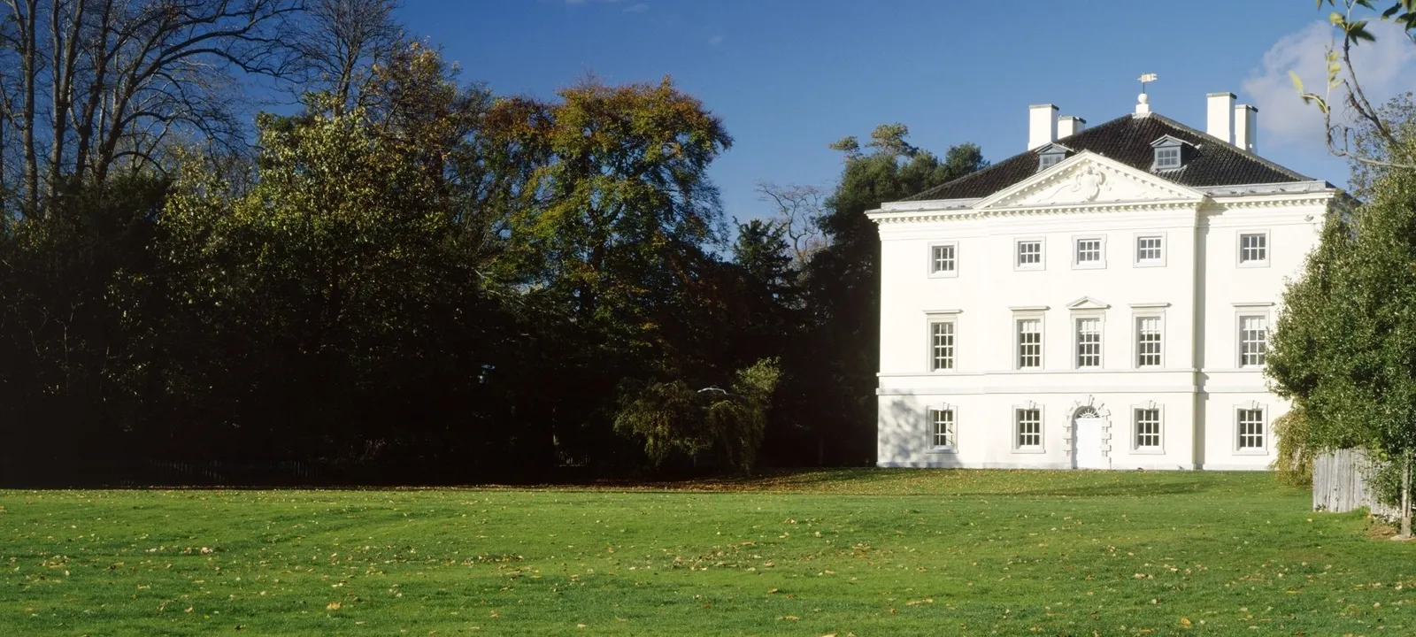 Marble Hill's white villa in autumn sunshine across a leaf-strewn lawn, with dark trees and a blue sky